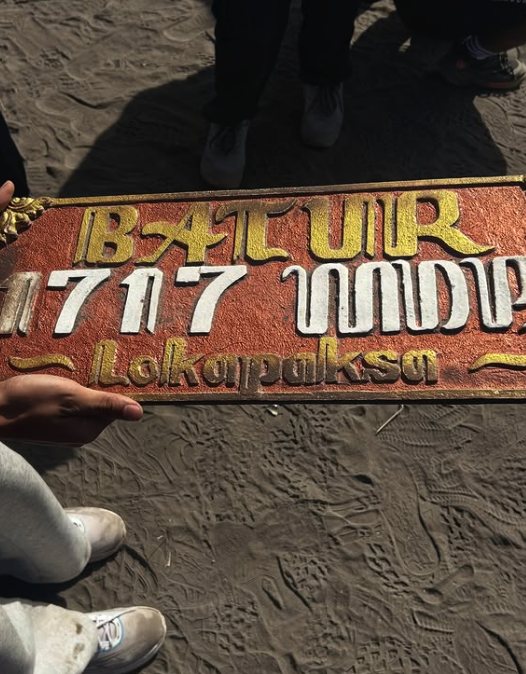 The painted Batur 1717 M sign held up over black volcanic sand at the top