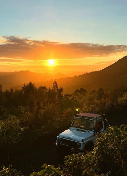 A blue 4WD jeep on the Mount Batur track as the sun comes up behind the ridge