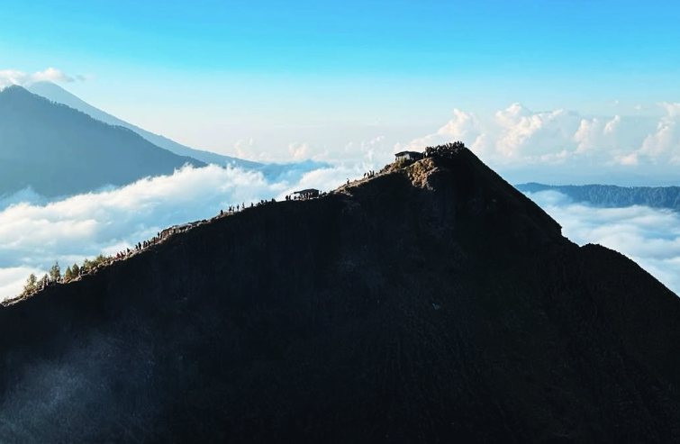 The Mount Batur summit ridge from the air, with a line of walkers strung along the path above the cloud