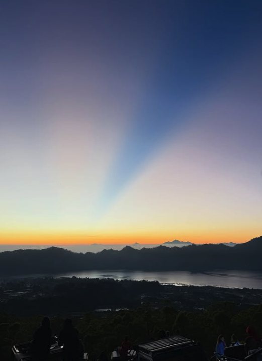 Dawn light fanning across the sky above Lake Batur, seen from the crater rim